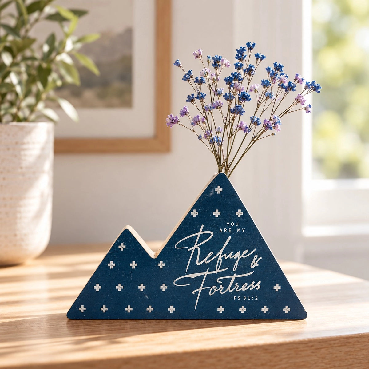 Refuge and Fortress Psalm 91:2 navy blue mountain-shaped wooden flower vase with purple and blue dried flowers on a wooden tabletop.