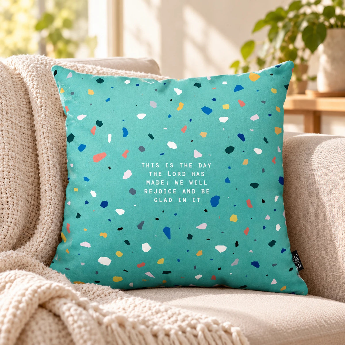 Rejoice and Be Glad Christian turquoise terrazzo cushion cover styled on a neutral sofa in a bright living room