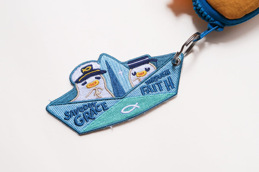 Saved by Grace Through Faith embroidered Christian keychain shaped like a paper boat with cute sailor characters attached to a bag zipper.