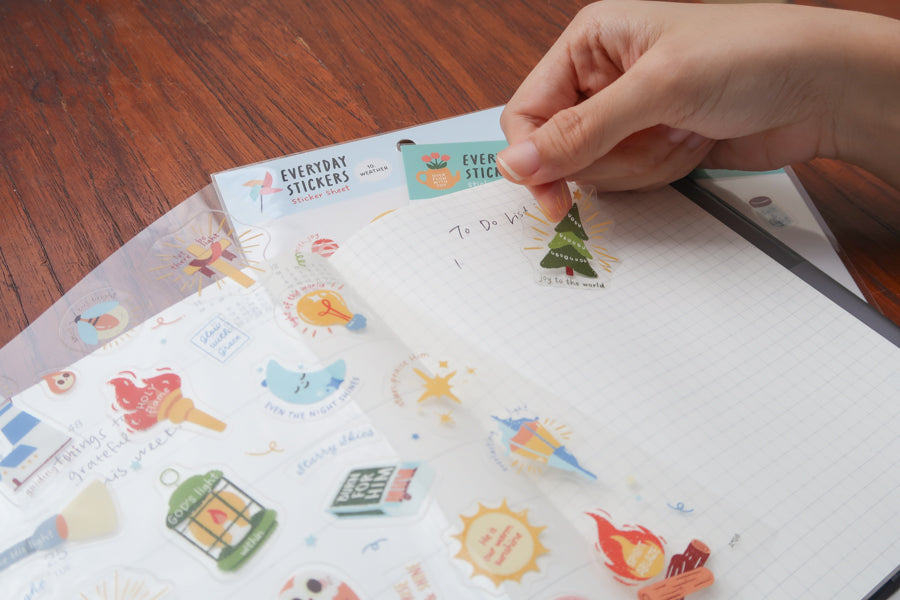 Person writing in planner with everyday believer self-care themed Christian sticker sheets underneath, showing gentle faith-based designs for daily reflection and encouragement