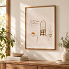 A framed minimalist line art poster with the script "As for me and my house, we will serve the Lord" hangs on a wall above a rustic wooden console table in a sunlit room.
