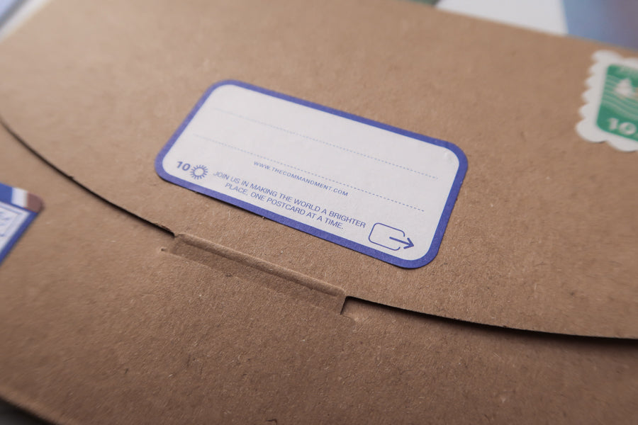 A close-up of a brown envelope with a label reading, "Join us in making the world a brighter place, one postcard at a time," encouraging positivity and connection through postcard sharing.