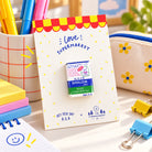 Shalom Pas Love Supermarket Christian pin displayed in a colourful desk lifestyle setting.