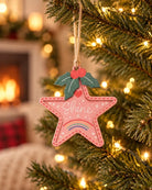 Pink star-shaped Shine Christmas tree bauble hanging from a warmly lit Christmas tree.