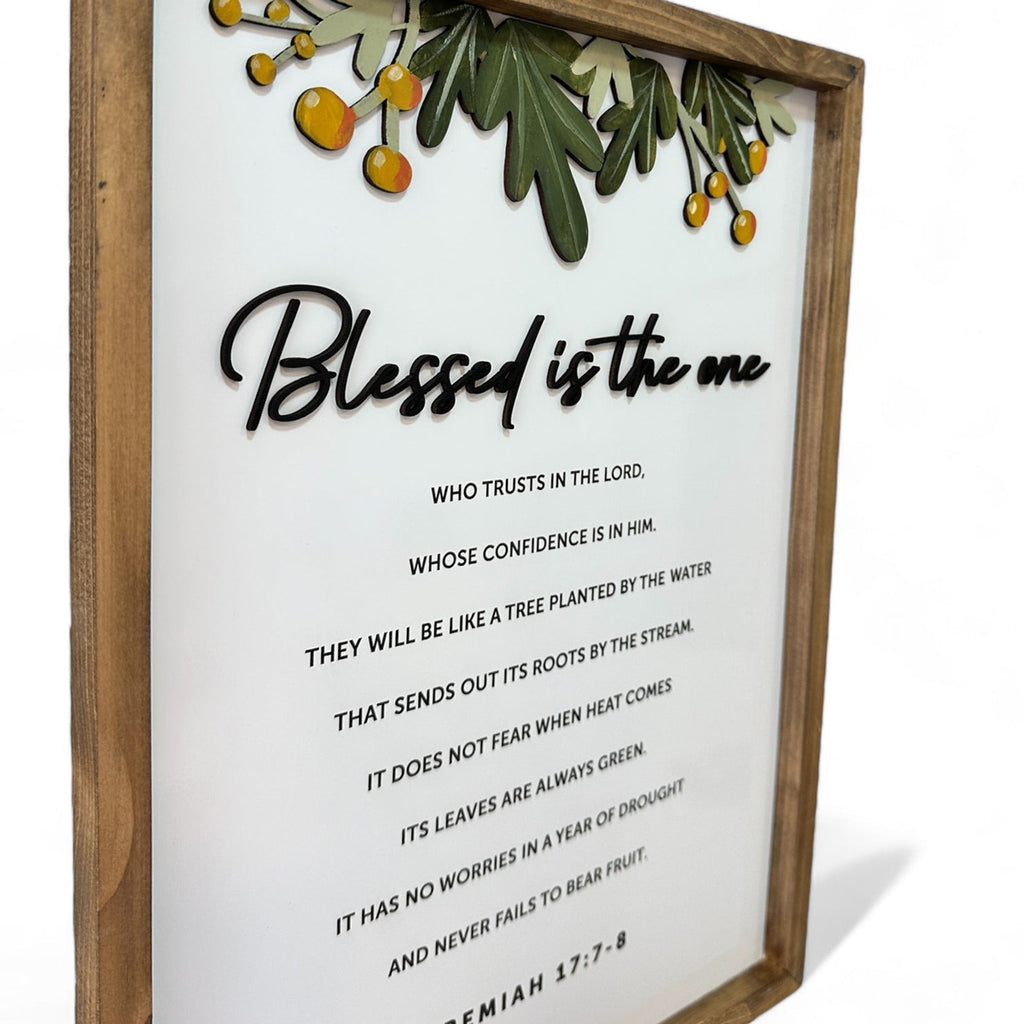 Side view of framed Bible verse wall art featuring Jeremiah 17:7-8 with the phrase 'Blessed is the one' and decorative greenery with orange accents.