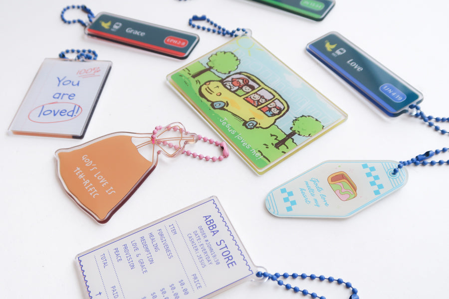 Singapore-inspired Christian acrylic keychain collection featuring Jesus Loves Me transport card, Grace and Love MRT sign designs, Abba Store receipt, and faith-filled reminders
