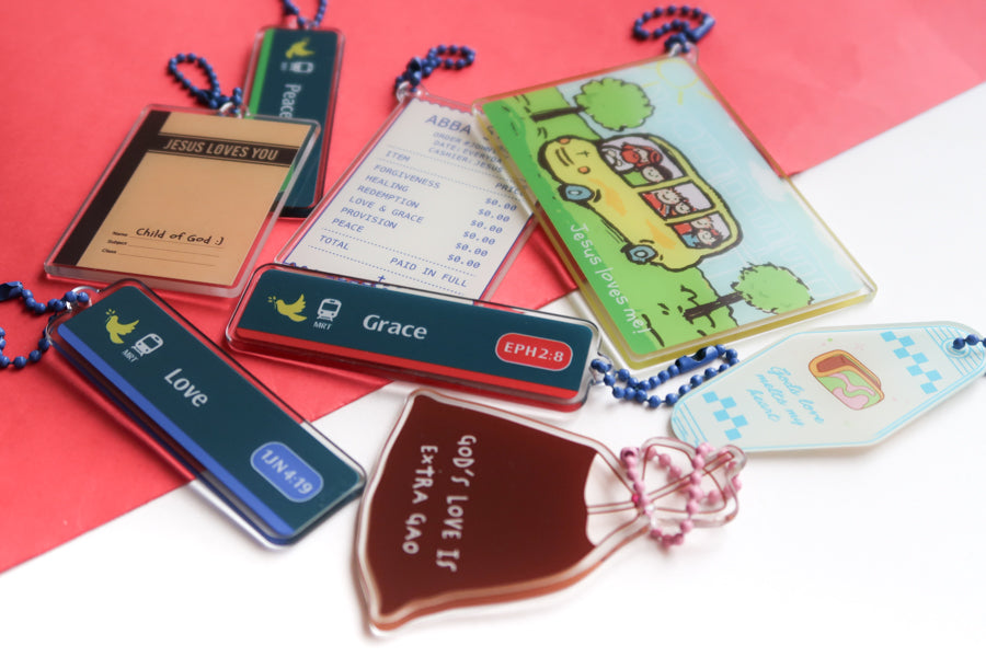 Singapore-inspired Christian acrylic keychain collection featuring Jesus Loves Me transport card, Grace and Love MRT sign designs, Abba Store receipt, and faith-filled reminders