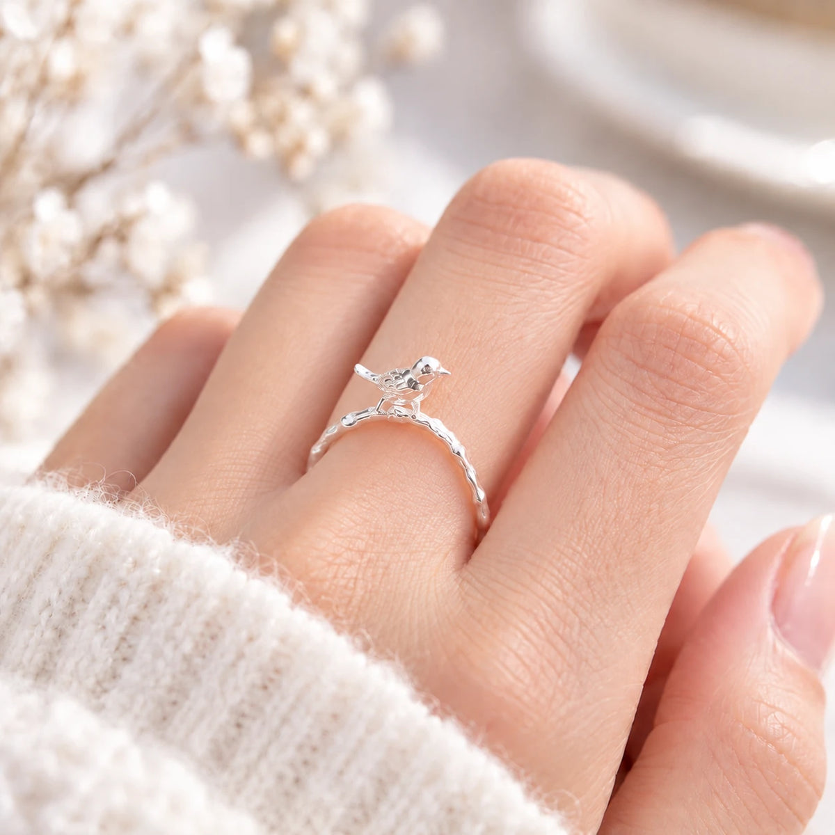 Close-up of a delicate silver Singing Bird ring worn on a finger, with a small bird perched on its branch-inspired band.