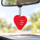 Love Never Fails red heart scent tag hanging from a car rear-view mirror