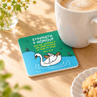 Strength and Honour swan and cygnets Christian coaster holding a coffee mug at a café table