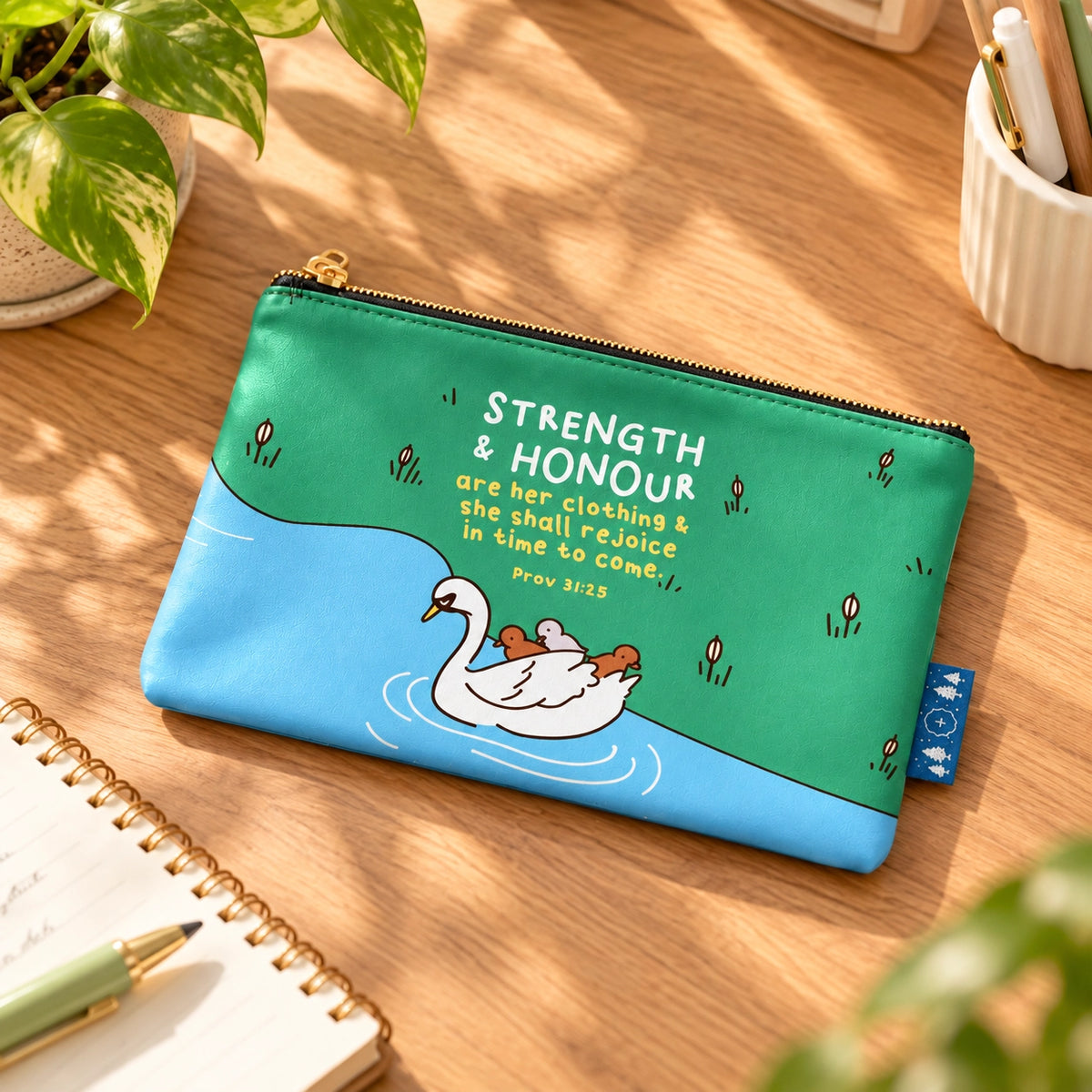 Strength and Honour Christian pouch featuring Proverbs 31:25 laid flat on a warm wooden desk in natural sunlight.