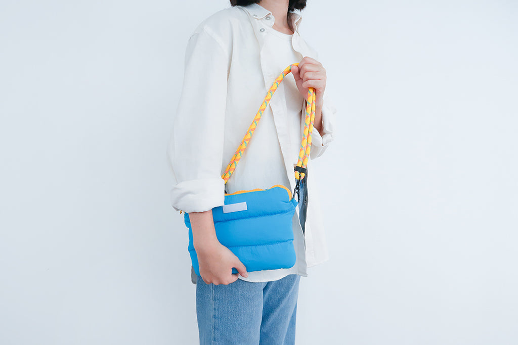 Model carrying the Cyan Pong Pong Bag, highlighting the bag's lightweight design with a sturdy yellow strap.