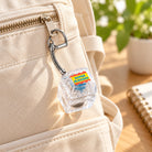 Super Blessed clear light-up keycap keychain clipped to cream canvas backpack in warm sunlight