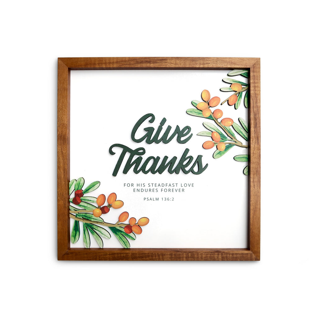 A wooden-framed wall art featuring the phrase "Give Thanks" with the scripture reference Psalm 136:2. Decorated with vibrant illustrations of green leaves and orange berries, the design emphasizes gratitude and God's steadfast love, perfect for Christian home decor.