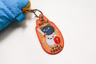 Embroidered Christian warrior cat keychain with “The Battle Is The Lord’s” text, featuring sword and cross shield on orange background.