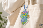 The Good Fruit acrylic keychain with blue ball chain clipped onto a canvas tote bag, designed by Thir.st in collaboration with The Commandment Co.