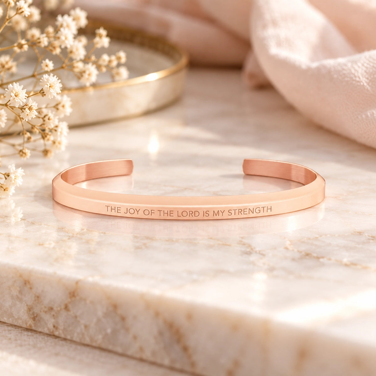 Rose gold The Joy of the Lord Is My Strength classic verse band displayed on a softly lit marble surface.