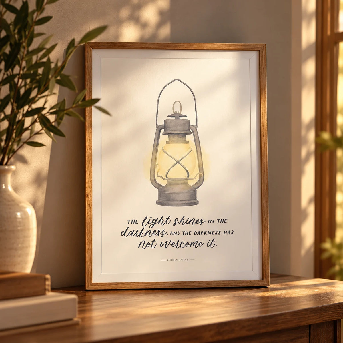 The Light Shines in the Darkness lantern Bible verse poster in a wooden frame on a sunlit shelf