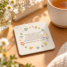 The Lord is Good Christian coaster styled on a sunlit wooden table beside tea and flowers.