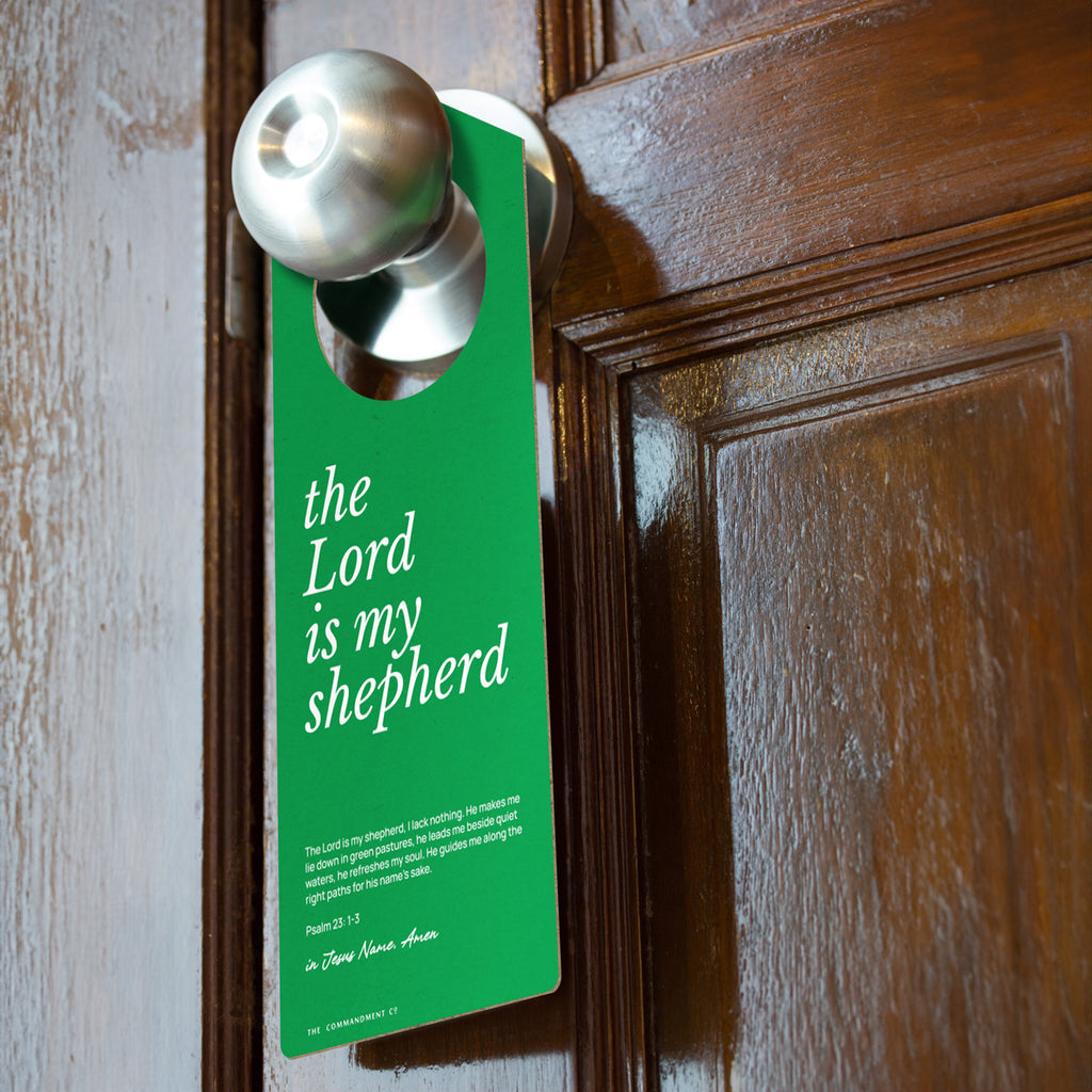 Green Christian door hanger featuring the text 'The Lord is my shepherd' with Psalm 23:1-3, hanging on a silver doorknob on a wooden door.