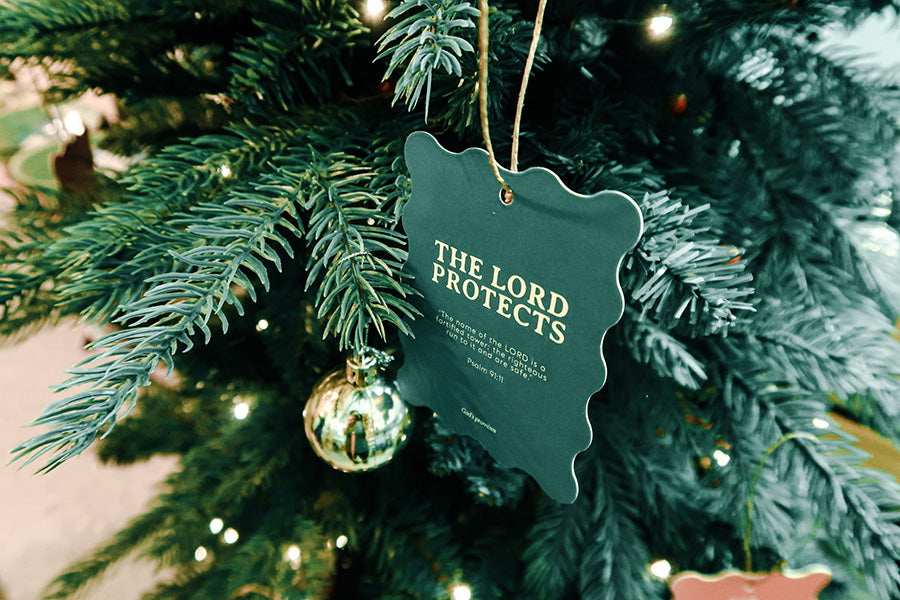 Christian Christmas tree hanging ornament featuring the Bible verse 'The Lord Protects' from Psalm 91:11, with a green scalloped design hanging on a decorated tree.