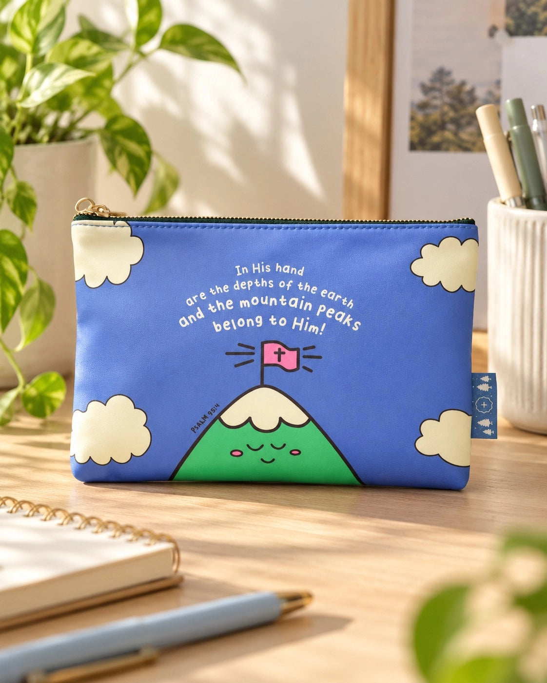 The Mountain Peaks Belong to Him blue Christian pouch displayed on a warm sunlit desk.