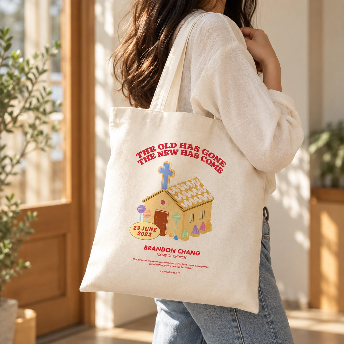 The New Has Come customisable baptism tote bag carried over the shoulder in a bright sunlit interior.