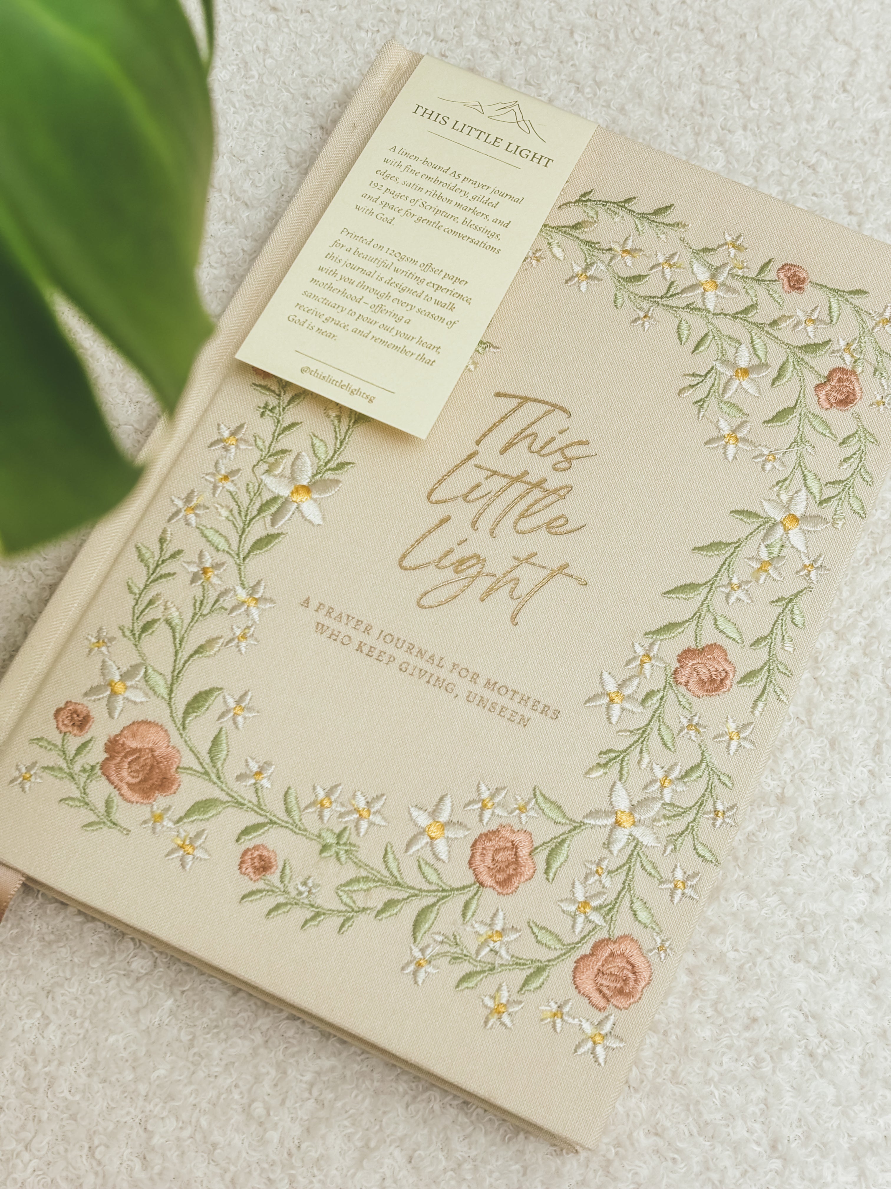 This Little Light floral prayer journal for mothers styled on a white chair with ribbon bookmarks