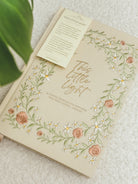 This Little Light floral prayer journal for mothers styled on a white chair with ribbon bookmarks