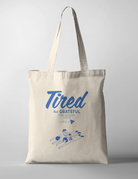 Tote Bag with the phrase "Tired But Grateful" featuring an illustration of parents lying down with two kids on them — a heartfelt design celebrating parenthood and faith.