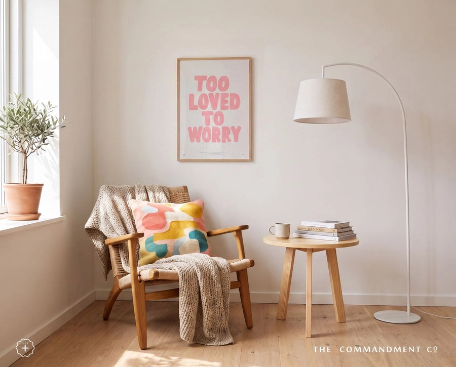 Too Loved to Worry Christian poster displayed above a cosy reading chair in a warm neutral room