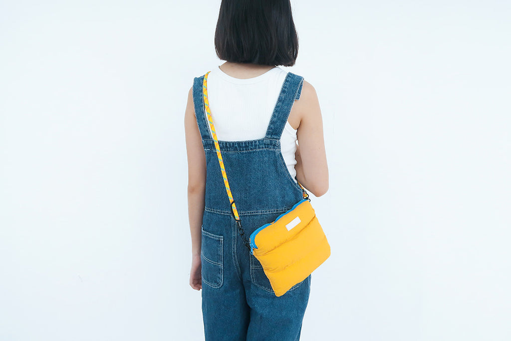 The Yellow Pong Pong Bag worn crossbody style, highlighting its stylish and functional design with a blue zipper accent.