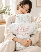 Woman hugging Trust In The Lord cross plush toy in a warm living room.