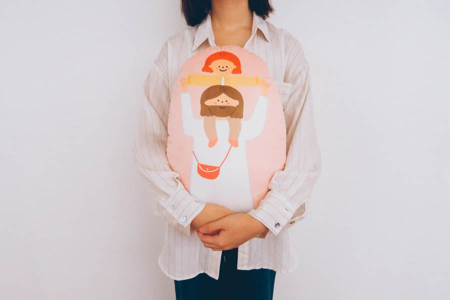 Person holding a soft, comforting plush toy with an illustration of Jesus lifting a child, labeled 'Held High by His Love' as a symbol of support and love.