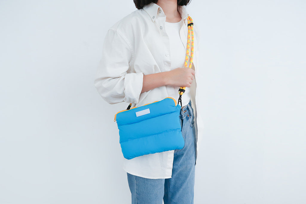 Cyan pong pong bag worn with a yellow-accented strap, designed for everyday use and style.