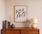 Walk By Faith Christian poster framed above a wooden cabinet in a warm neutral home interior