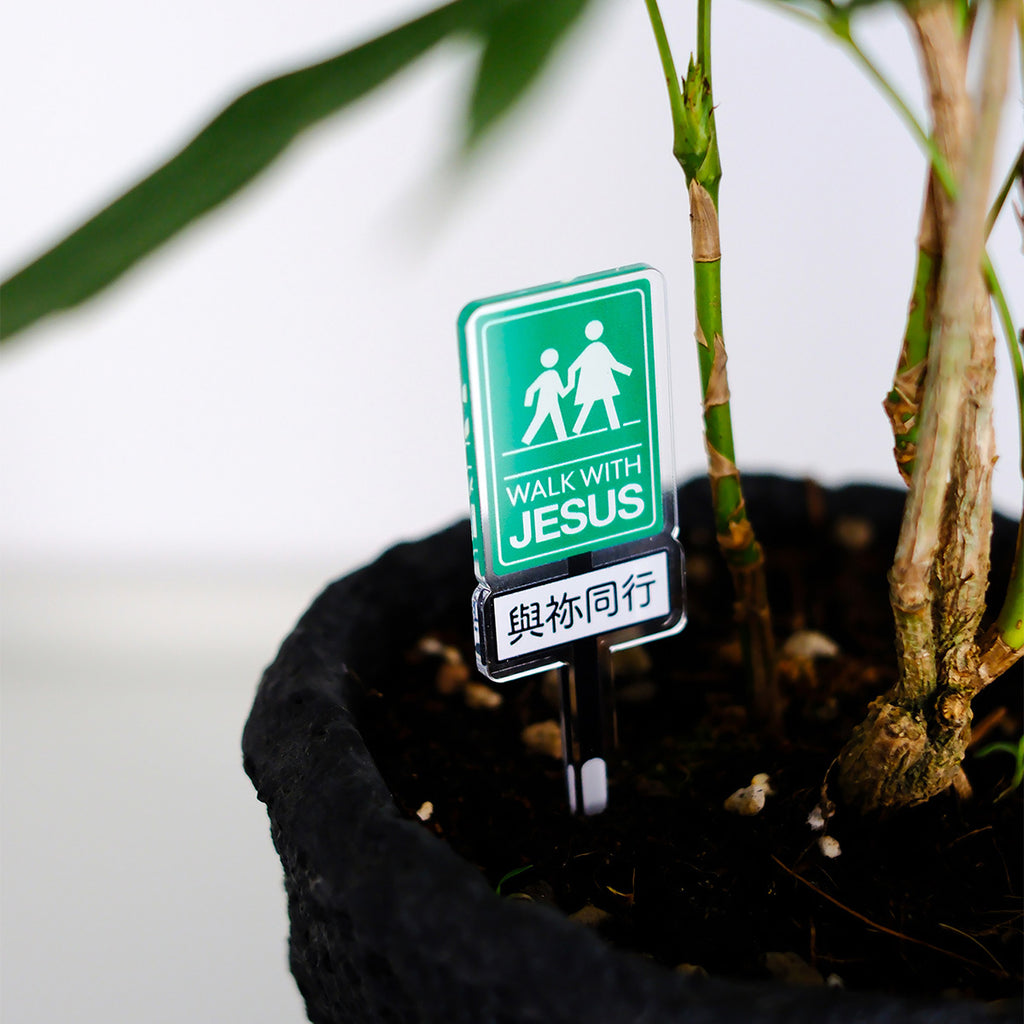 Green acrylic sign with the message 'Walk with Jesus' placed in a plant pot, symbolizing Christian faith and spiritual inspiration.