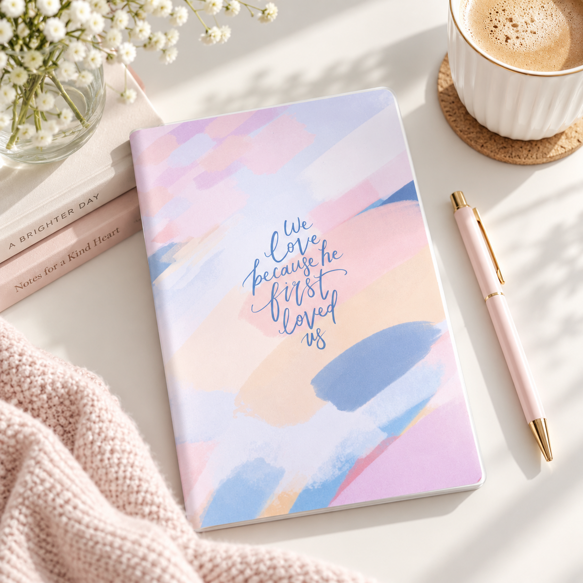 We Love Because He First Loved Us A5 Christian notebook styled on a bright desk with coffee, flowers and a pen.