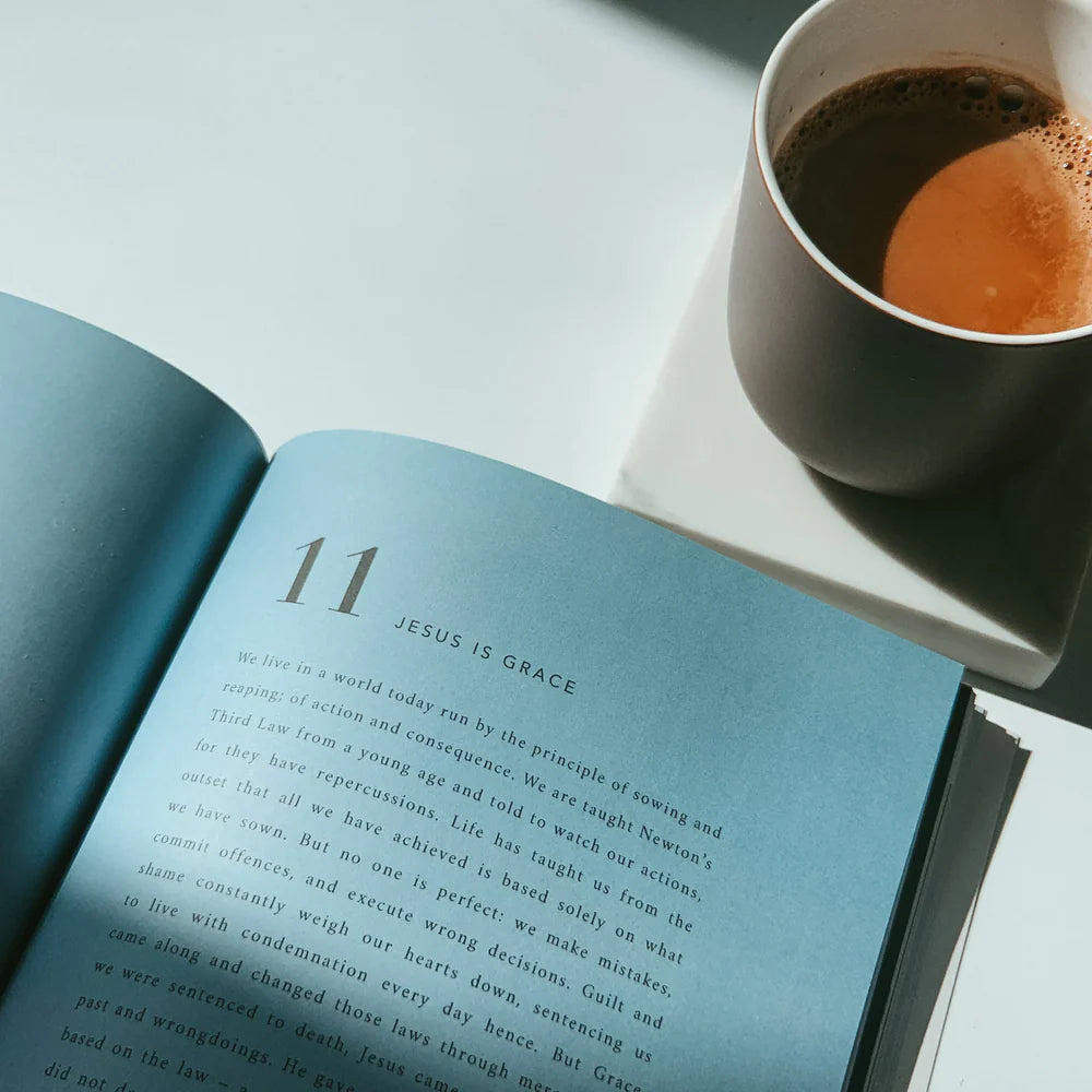 Open Who Is Jesus book displaying the chapter "Jesus Is Grace" beside a warm cup of coffee, inspiring simple happiness and reflection on faith and grace.