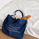 Navy canvas tote bag featuring the message “Today is gonna be a wonderful day, for God has blessed me,” filled with books and a baguette
