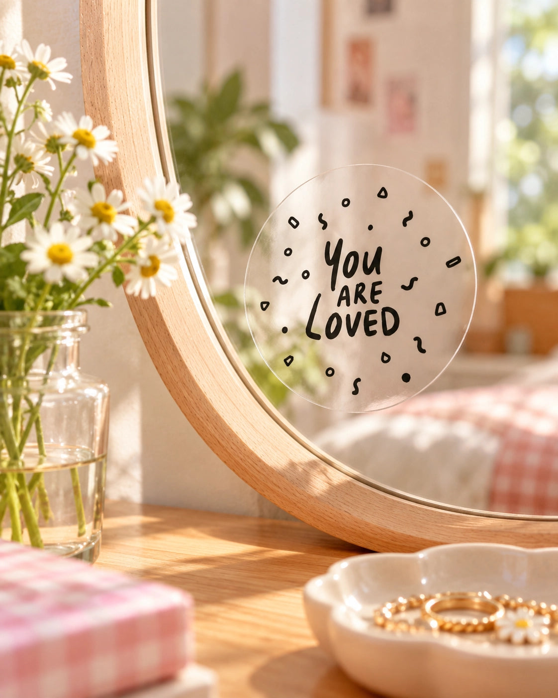 You Are Loved transparent mirror decal sticker applied to a round wooden-framed mirror in a warm bedroom setting.