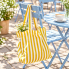 Yellow and white striped You Are My Light canvas tote bag hanging on a blue outdoor café chair