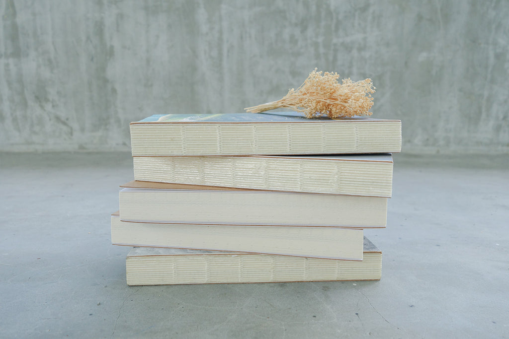 Side view of 5 books stacked together with gold dried flowers as decoration