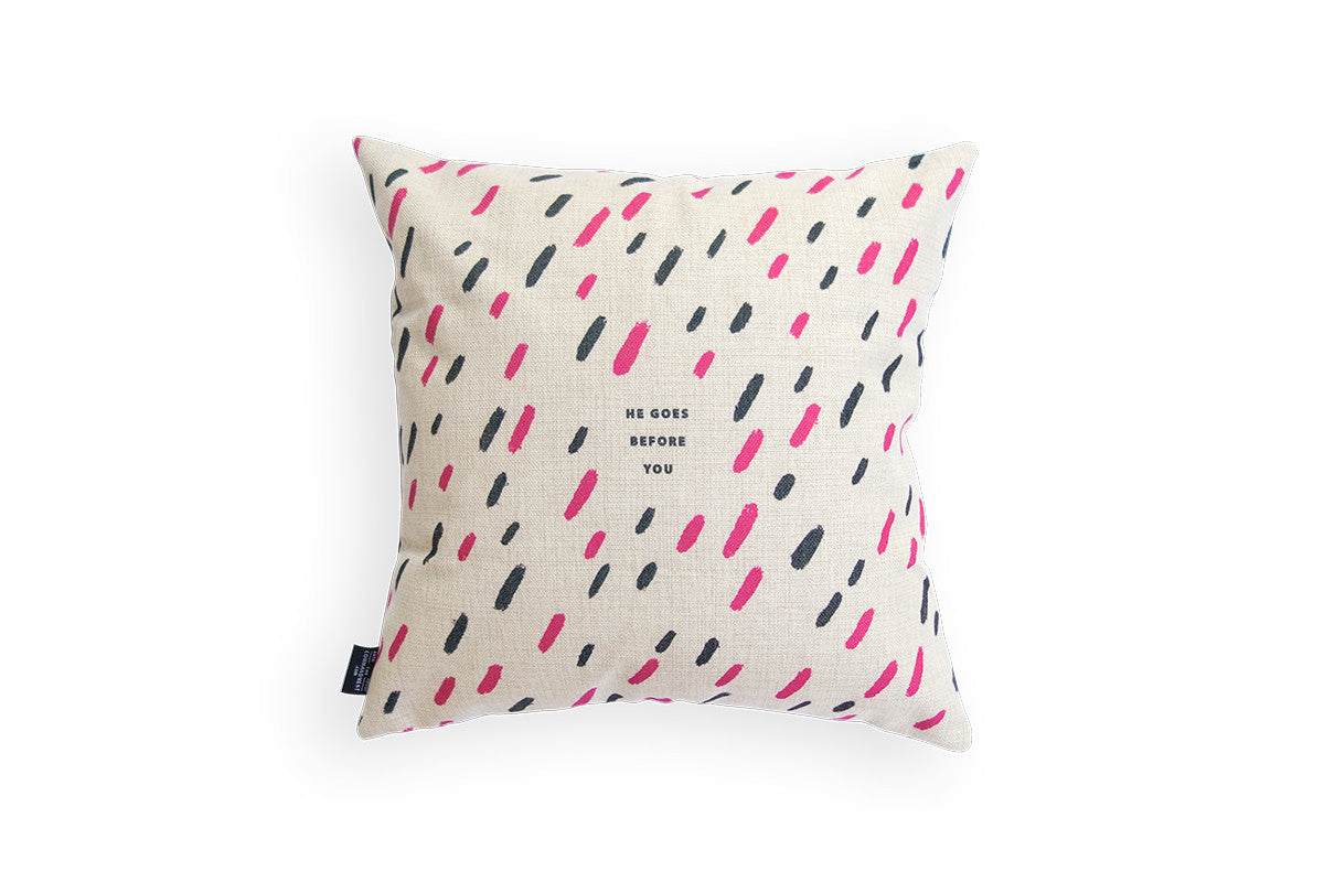 The back of pillow cover features cream background and black and pink brush swatches. The verse is 'He goes before you'