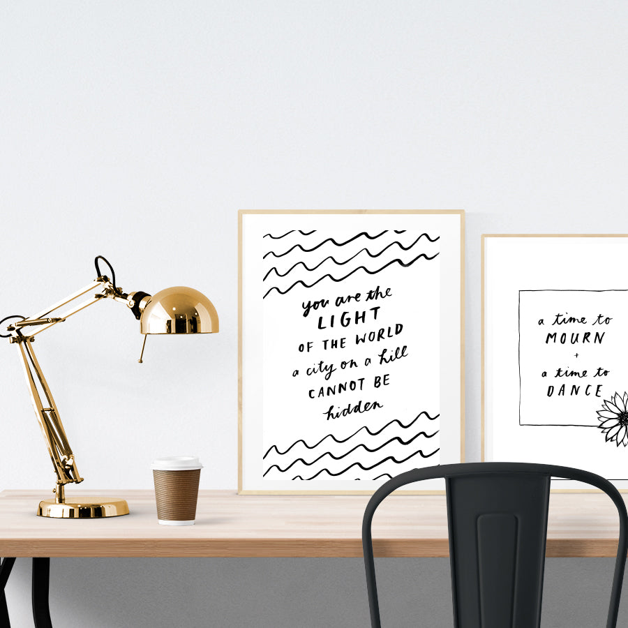 A3 beautiful calligraphy poster placed standing next to a smaller A4 sized calligraphy poster on a wooden table. Minimalistic Christian home interior design ideas.