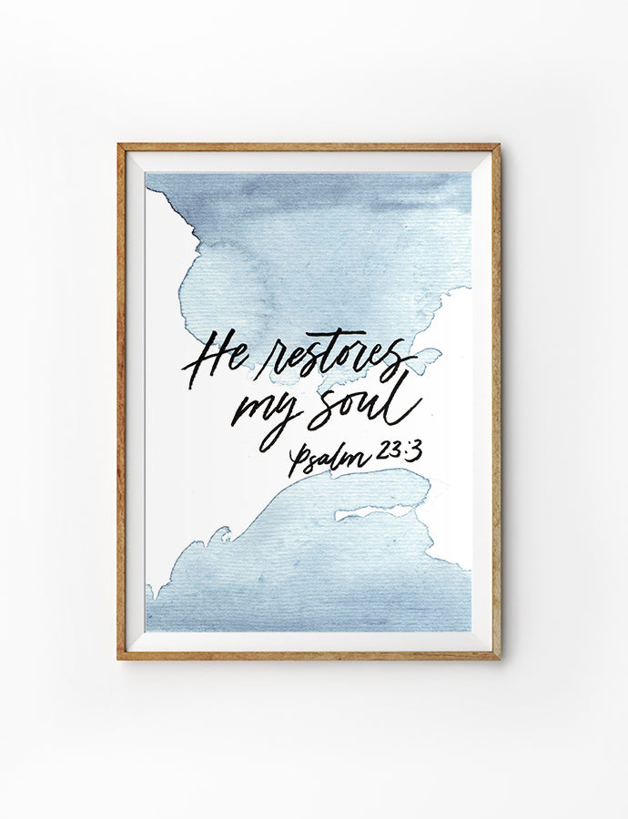 Poster featuring beautiful typography bible verses with water colour designs ‘He restores my soul’ is hung on the wall in a gold photo frame’. 200GSM paper, available in A3,A4 size.