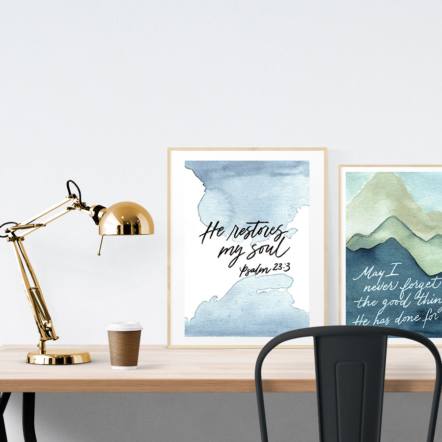 A3 beautiful calligraphy poster placed standing next to a smaller A4 sized mountains painting poster on a wooden table. Inspiring home decor ideas.