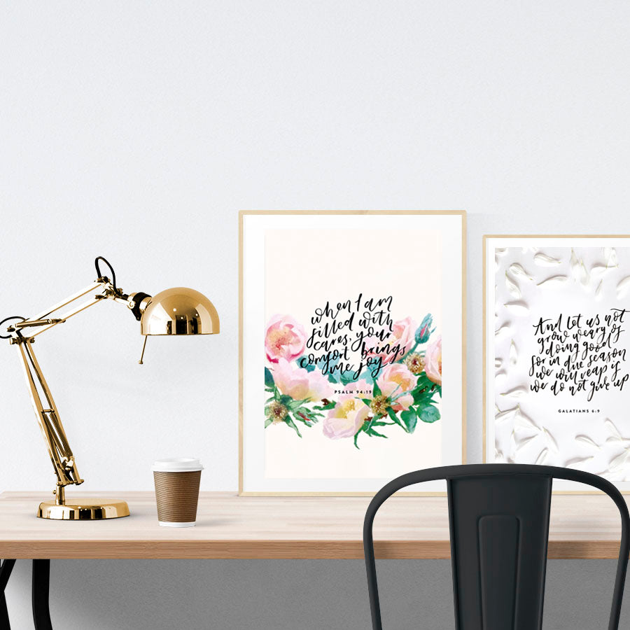 A3 beautiful calligraphy poster placed standing next to a smaller A4 sized calligraphy poster on a wooden table. Minimalistic Christian home interior design ideas.
