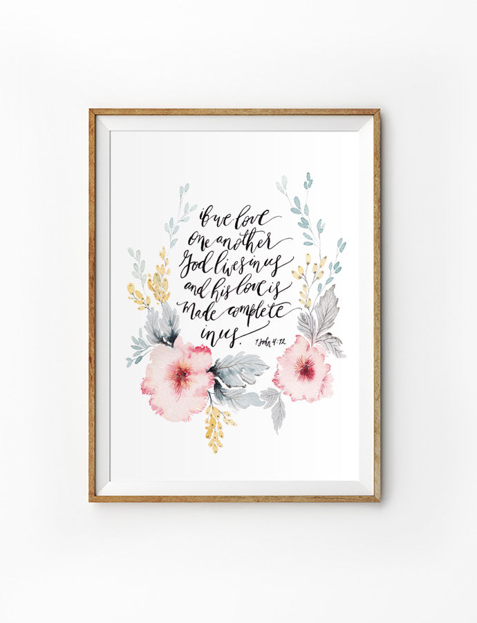 Poster featuring beautiful typography bible verses with flower wreath designs ‘but love one another God lives in us and his love is made complete in us’ is hung on the wall in a gold photo frame’. 200GSM paper, available in A3,A4 size.