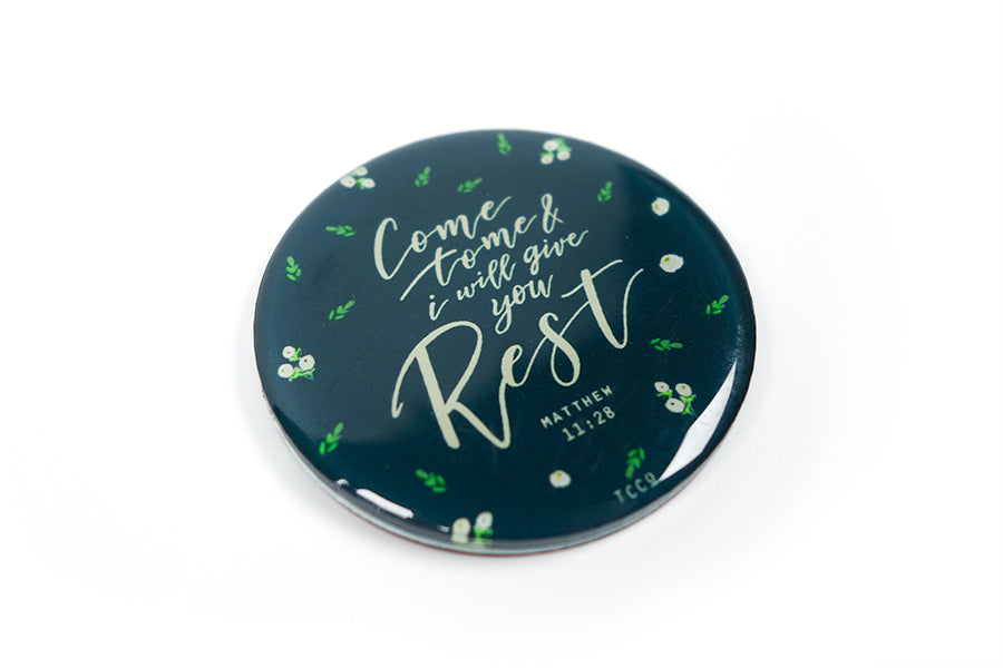 Close up of 5.5 cm diameter circular Acrylic fridge magnet with bible verse “Come to me and I will give you rest” on foliage background.
